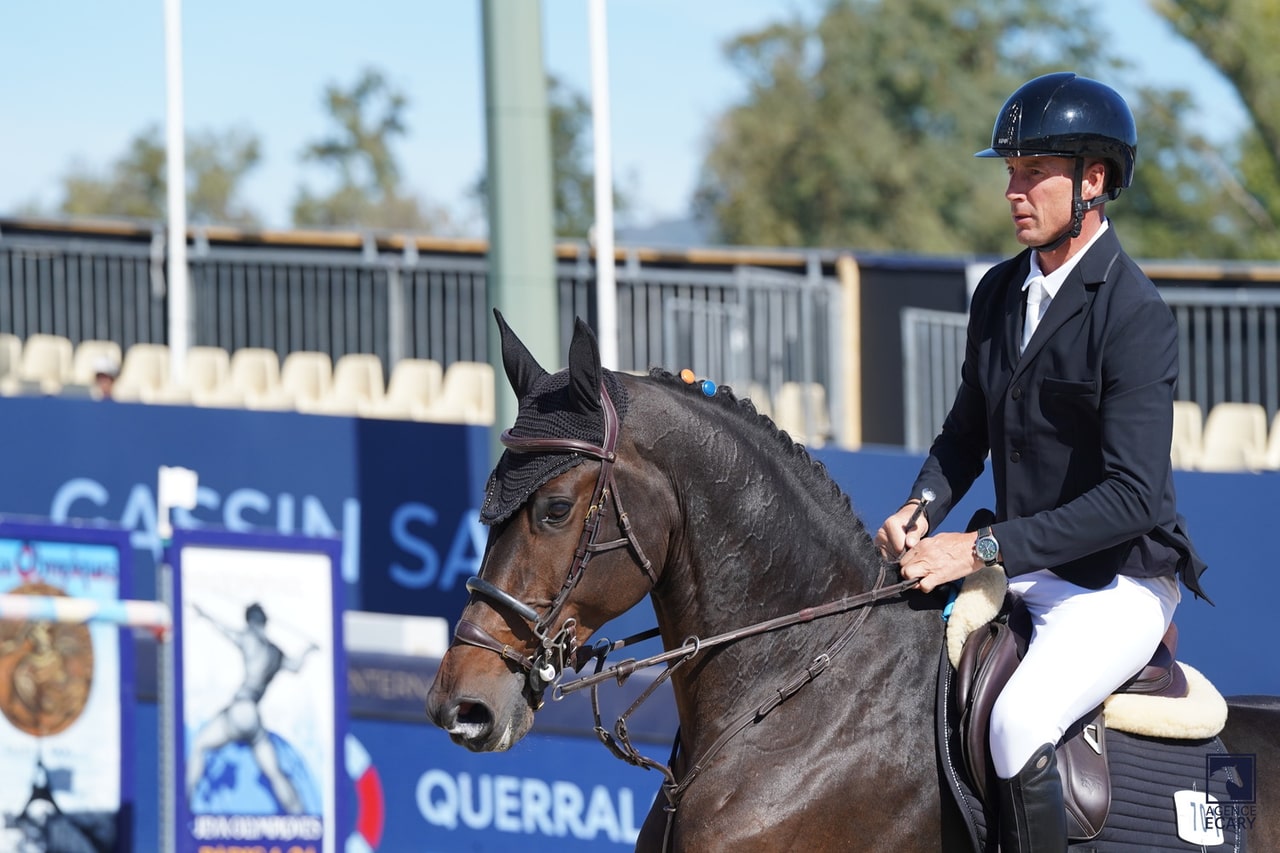 Alain Jufer riding a horse with orange and blue jewellery in its braided mane