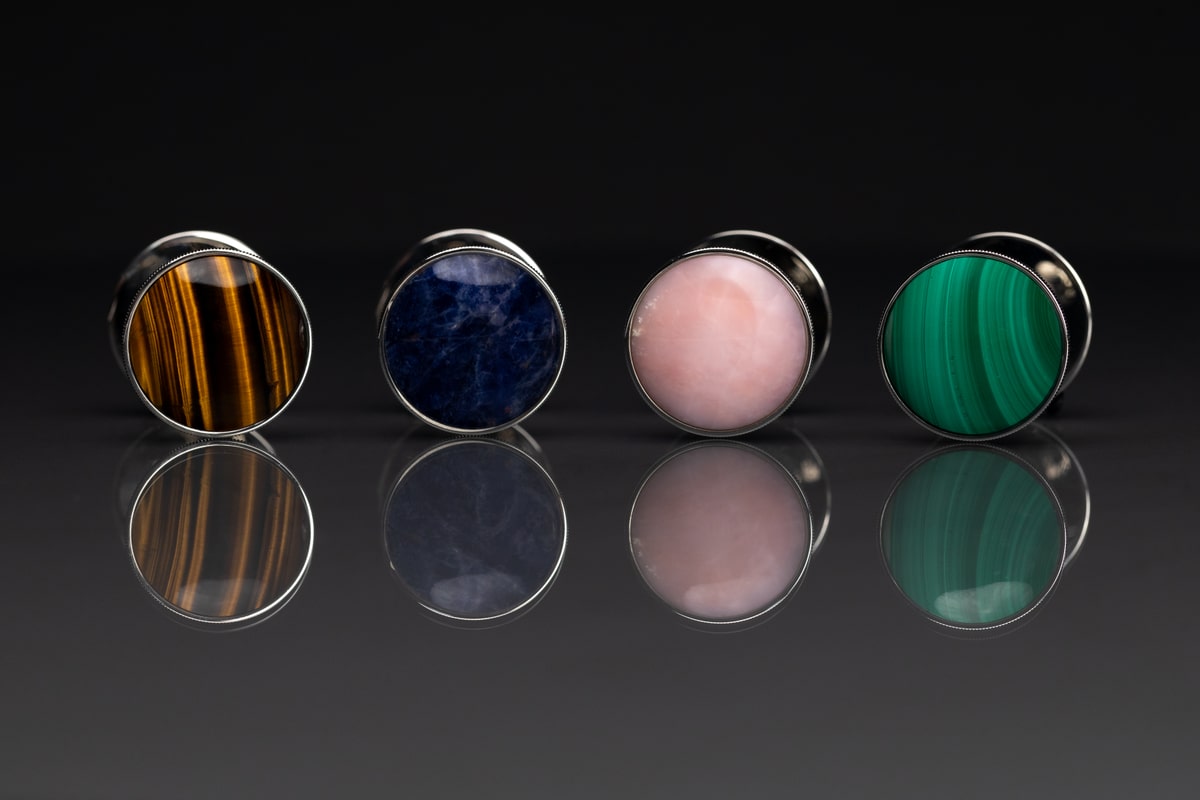 Tiger’s Eye, Blue Sodalith, Pink Opal and Green Malachite pins with their reflections on a dark studio background
